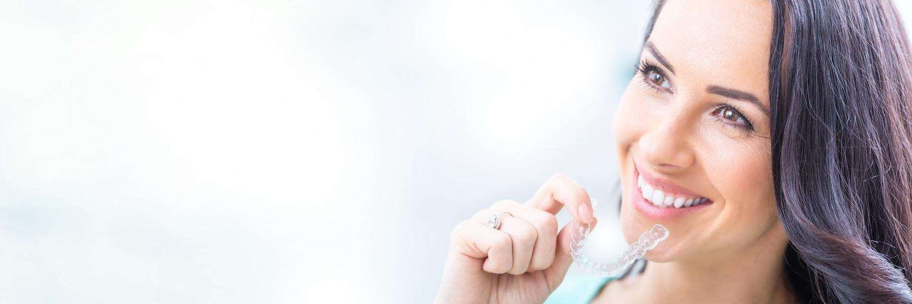Woman smiling with clear aligner in her hand, Roseville NSW